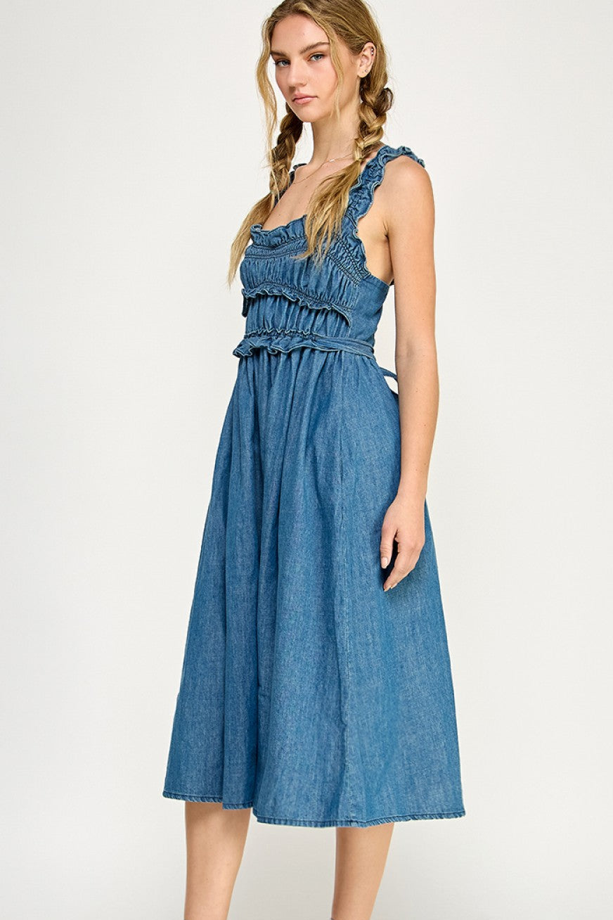 Smocked denim midi dress with ruffled straps, tiered bodice, and side pockets, styled with white sneakers.