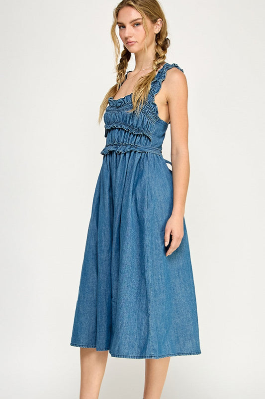 Smocked denim midi dress with ruffled straps, tiered bodice, and side pockets, styled with white sneakers.