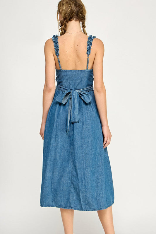 Smocked denim midi dress with ruffled straps, tiered bodice, and side pockets, styled with white sneakers.