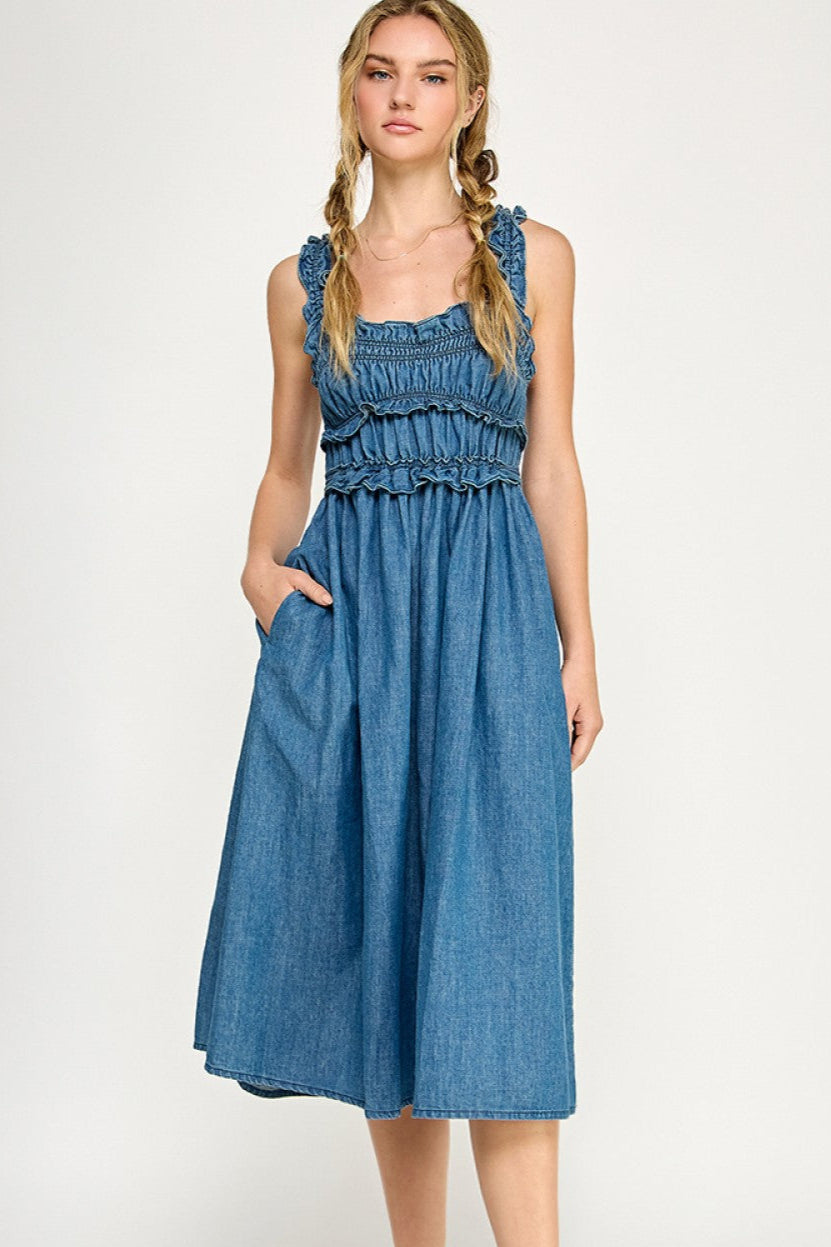 Smocked denim midi dress with ruffled straps, tiered bodice, and side pockets, styled with white sneakers.